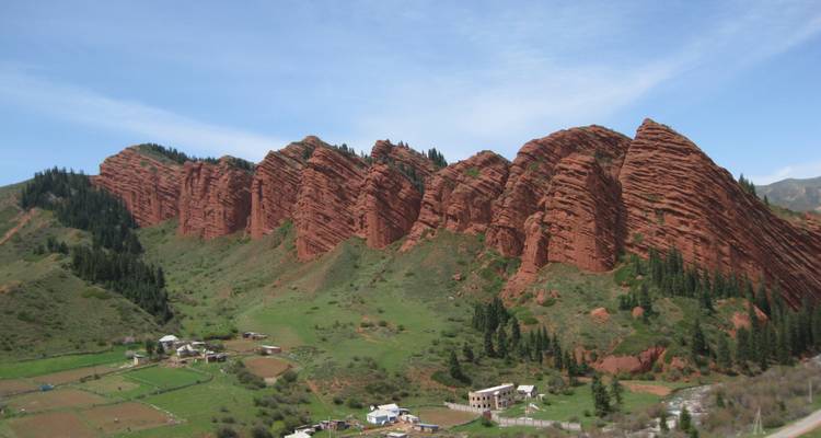 Falaises de grès rouge de Jeti-Oguz s'élevant au-dessus de pâturages verts et de petites maisons de village