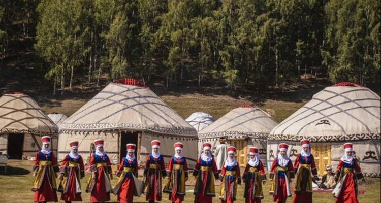 Rangée de femmes kirghizes vêtues traditionnellement debout devant des yourtes en feutre dans un camp culturel