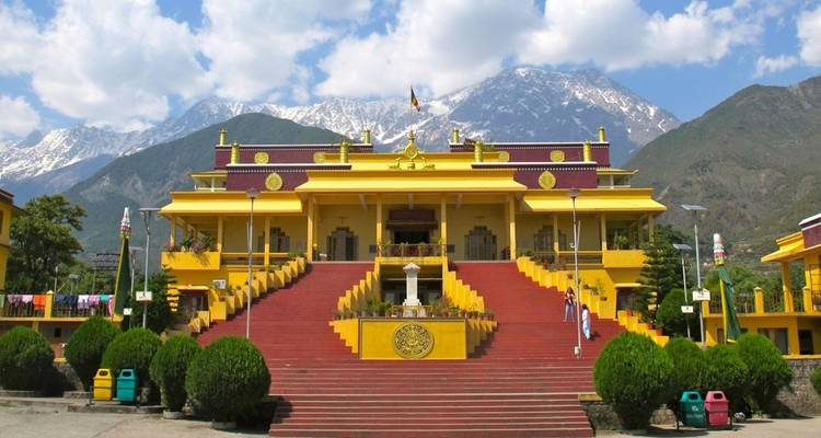 Een helderrood klooster met zwierige rode trappen ligt onder besneeuwde bergtoppen en blauwe lucht.