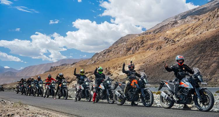 Reihe von Abenteuerfahrern auf Motorrädern posiert mit Daumen hoch entlang einer malerischen Wüsten-Bergstraße.