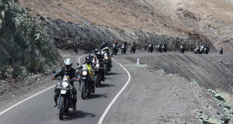 Lange Schlange von Motorradfahrern windet sich entlang einer kargen Himalaya-Straße, die in felsiges Gelände geschlagen wurde.