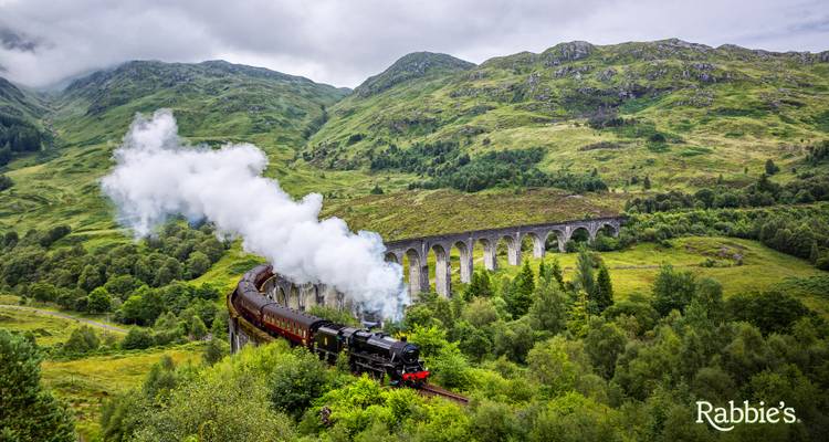 Stoomlocomotief die over het Glenfinnan Viaduct kronkelt temidden van groene Highlands met een rookpluim