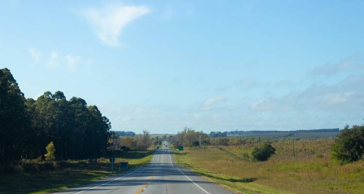 Leere zweispurige Landstraße erstreckt sich gerade zum Horizont durch die grasbewachsene uruguayische Landschaft.