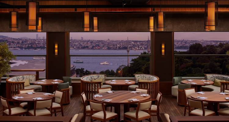 Elegantes Restaurantinneres mit runden Holztischen mit Blick auf den Bosporus in der Dämmerung.