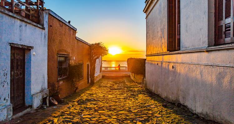 Goldenes Sonnenlicht erfüllt eine schmale Kopfsteinpflastergasse zwischen historischen Gebäuden, die zu einem Blick auf das Wasser führt.