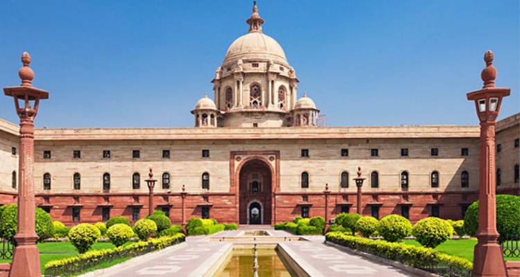 Gran Rashtrapati Bhavan con jardines simétricos y estanque reflectante bajo un cielo azul brillante de Delhi.
