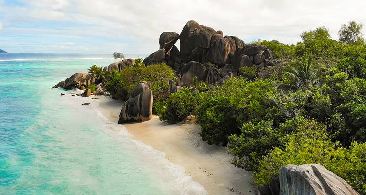 Plage tropicale de sable blanc avec une eau turquoise et des rochers de granit spectaculaires encadrés par une végétation luxuriante.