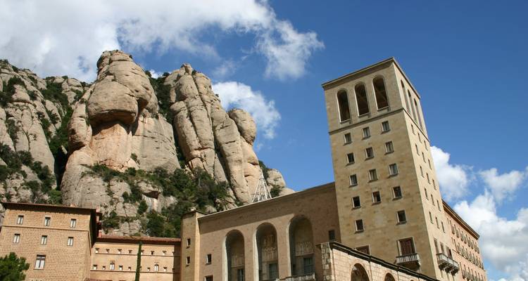 Bâtiments en pierre du monastère de Montserrat adossés à des formations rocheuses arrondies spectaculaires sous un ciel bleu éclatant.