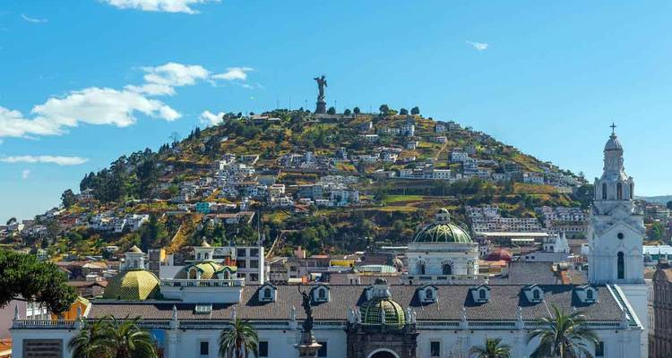 Panoramic view of Quito's El Panecillo hill crowned by the Virgin statue under blue sky.