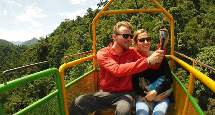 Couple taking a selfie while riding an open-air cable car above lush cloud-forest vegetation.