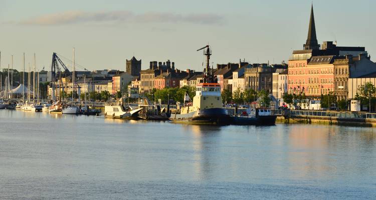 Quai de Waterford avec des navires amarrés et des bâtiments colorés au bord de la rivière éclairés par la douce lumière matinale.