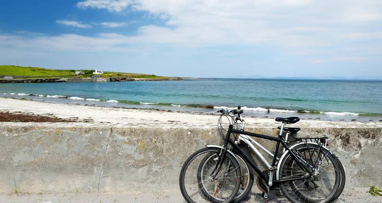 Deux bicyclettes sont appuyées contre un muret donnant sur une plage irlandaise tranquille et une mer bleue.