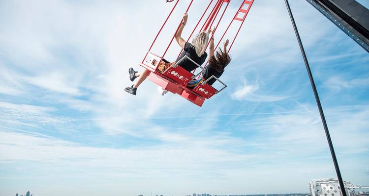 Deux amateurs de sensations fortes sur une balançoire de toit élevée s'élançant au-dessus de l'horizon d'Amsterdam.