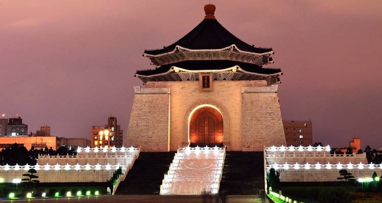 Mémorial en pierre blanche illuminé avec toit noir à gradins et grand escalier brillant au crépuscule.