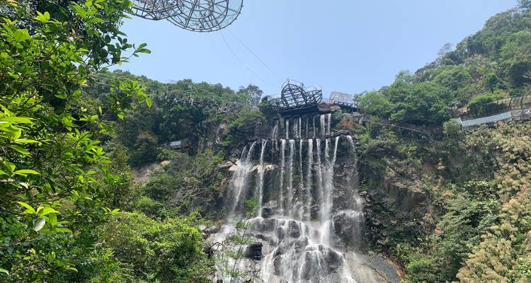 Hoge waterval stort naar beneden van een rotsige klif terwijl een glazen brugconstructie de kloof overspant boven weelderig groen.