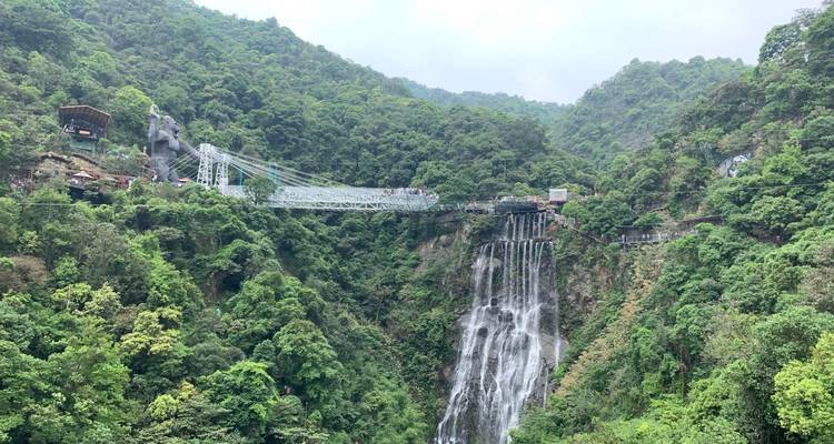Panoramisch uitzicht op een weelderige kloof met een hangende glazen brug en een waterval te midden van dicht bos.