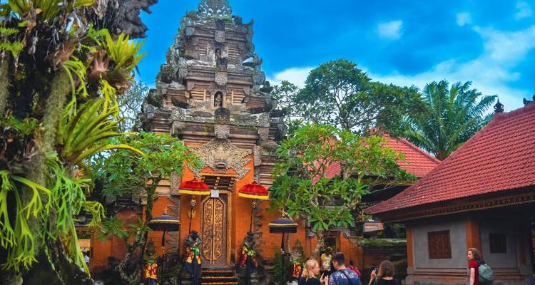 Visitors enter an ornate Balinese temple courtyard rich with carvings and colorful umbrellas.