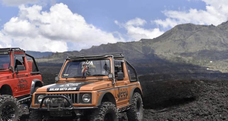 Off-road jeeps drive across dark volcanic lava fields beneath Mount Batur.