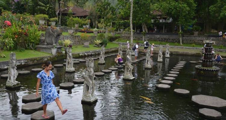 Visitors balance across stone stepping-stones over a koi pond in a lush garden.