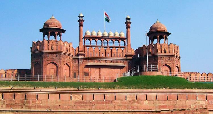 Las murallas de arenisca roja del Fuerte Rojo de Delhi coronadas con la bandera india contra el cielo azul.