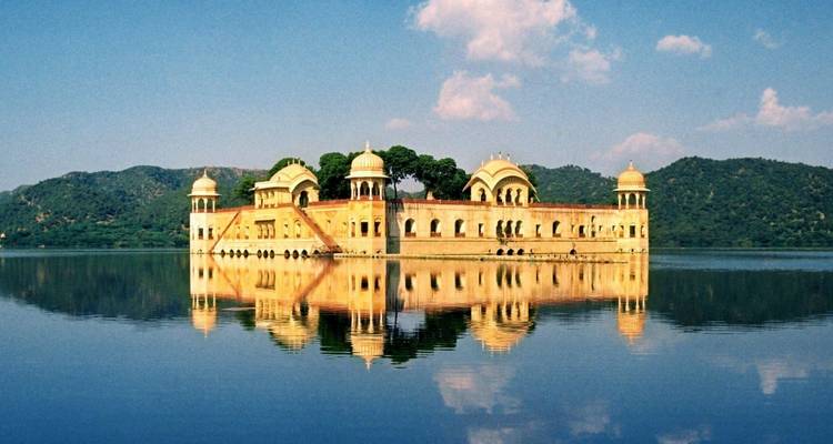 El palacio Jal Mahal junto al lago se refleja perfectamente en las aguas tranquilas contra un telón de fondo de colinas verdes.