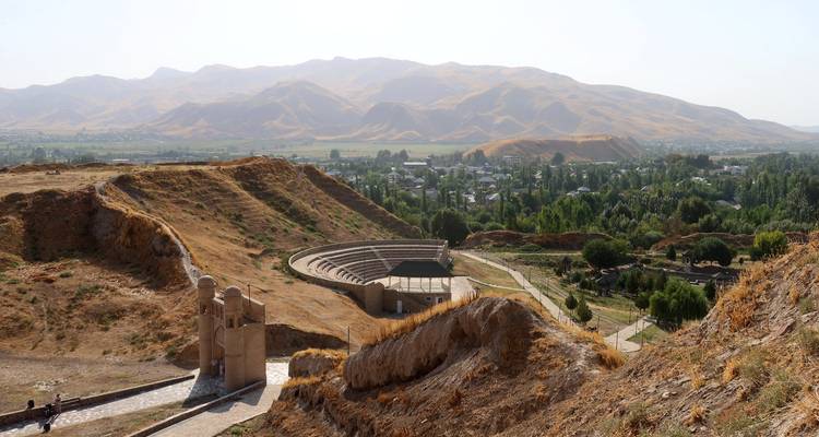 Ruinen eines antiken Amphitheaters auf einem Hügel überblicken ein fruchtbares Tal und ferne Berge.