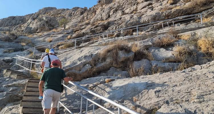 Reisende erklimmen steile Steinstufen, die in einen kahlen Berghang gehauen sind.