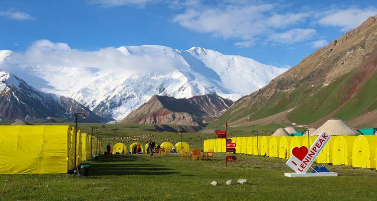 Leuchtend gelbe Expeditionszelte bilden ein Basislager unterhalb der verschneiten Flanke des Lenin-Gipfels.