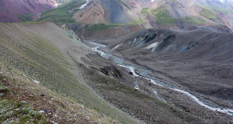 Erodiertes Tal aus losem Geröll und gewundenem Schmelzwasserstrom inmitten mehrfarbiger Hänge.