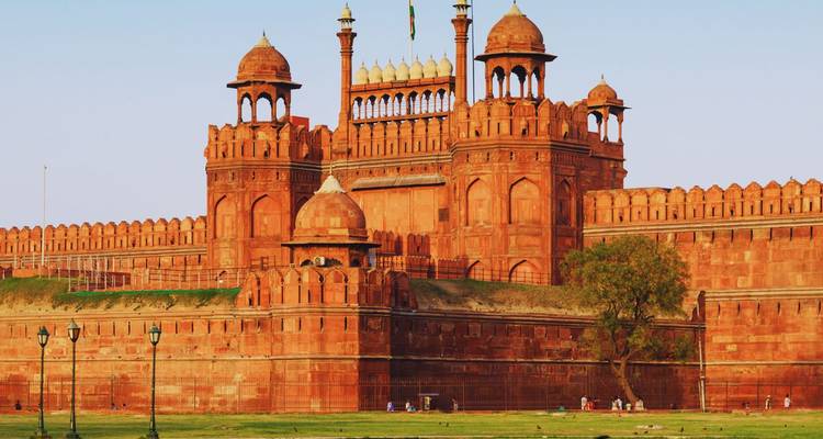 Imponentes muros de arenisca roja y cúpulas del histórico Fuerte Rojo de Delhi resplandeciendo bajo la luz del atardecer.
