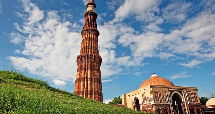 Torre del Qutub Minar elevándose y mezquita adyacente de arenisca ornamentada contra un cielo azul vívido.
