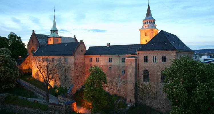 Les lumières du soir illuminent les tours de brique et les murs du château d'Akershus contre un ciel crépusculaire.