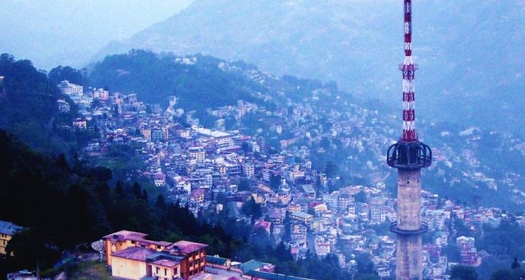 Hangseitenpanorama der Stadt Gangtok, die sich über bewaldete Hänge mit einem hohen Kommunikationsturm erstreckt.