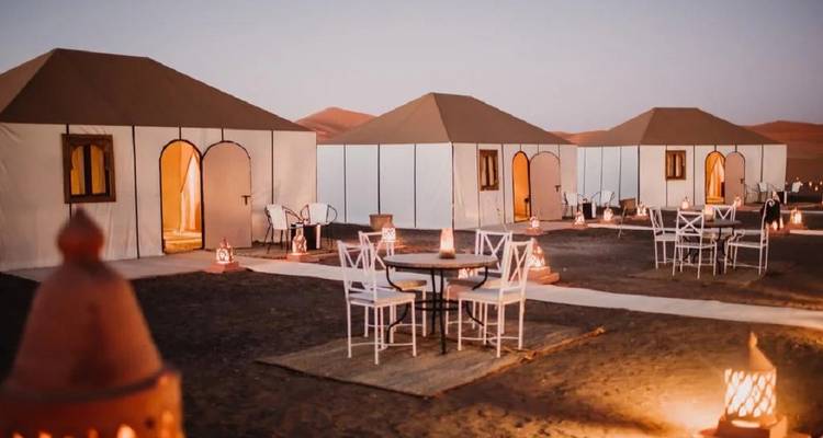 Tentes de toile avec sièges extérieurs et lanternes installées sur le sable noir du désert au crépuscule.