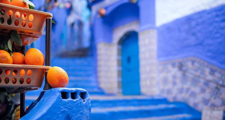 Des oranges vives empilées dans des plateaux en plastique contre les murs bleus éclatants et les marches carrelées de Chefchaouen.