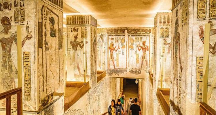 Decorated walls of an ancient Egyptian tomb corridor with tourists exploring.
