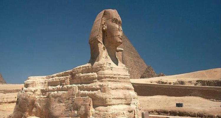 The Great Sphinx of Giza with a pyramid rising behind it against a deep blue sky.