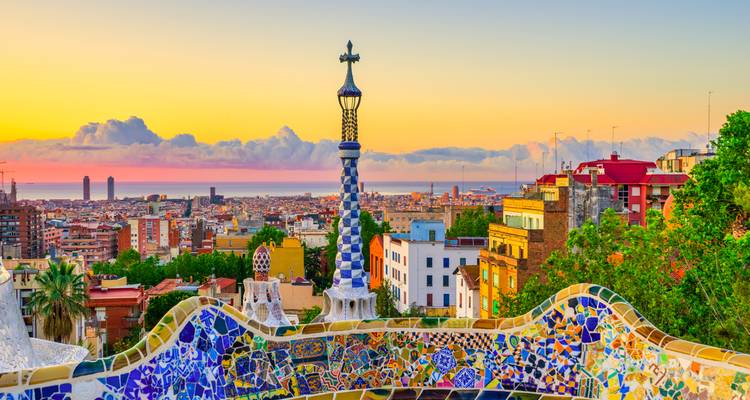 La terrasse de mosaïques colorées du Parc Güell surplombant Barcelone au lever du soleil avec la Méditerranée au loin.