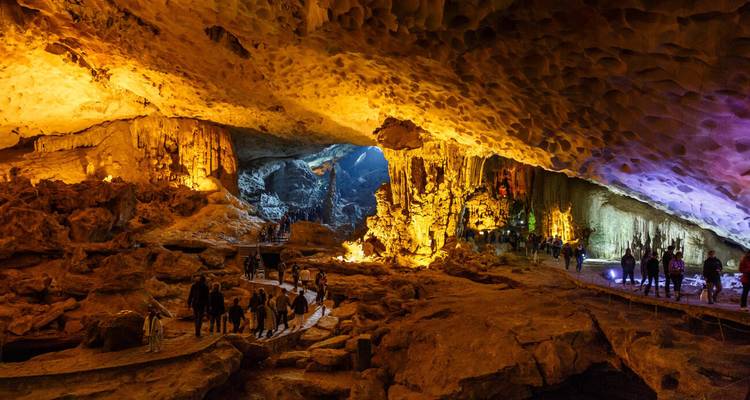 Illuminated limestone cavern with stalactites and a walkway of visitors exploring inside