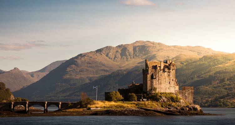 Eilean Donan Castle liegt auf einer kleinen Insel in einem ruhigen Loch, umrahmt von den schroffen Highlands zur goldenen Stunde.