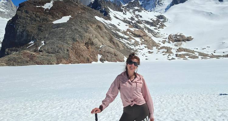 Excursionista sonriente se encuentra en una meseta nevada con picos rocosos y glaciares que se alzan detrás en la Patagonia.