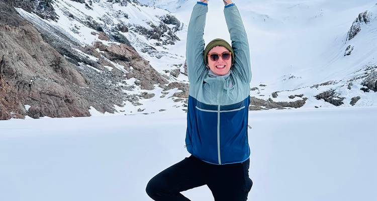 Un viajero practica una postura de yoga en un campo de nieve pristino en medio de un paisaje alpino escarpado.