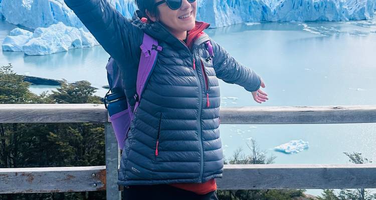 Mujer sonriente con los brazos extendidos en un balcón con vista al Glaciar Perito Moreno.