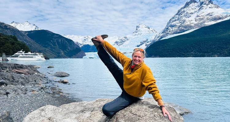 Viajero flexible realiza un estiramiento en split sobre una roca junto al lago con picos cubiertos de hielo detrás.
