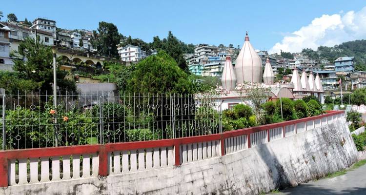 Straatbeeld van een Indiase bergstad met een wit tempelcomplex en woongebouwen onder blauwe luchten.