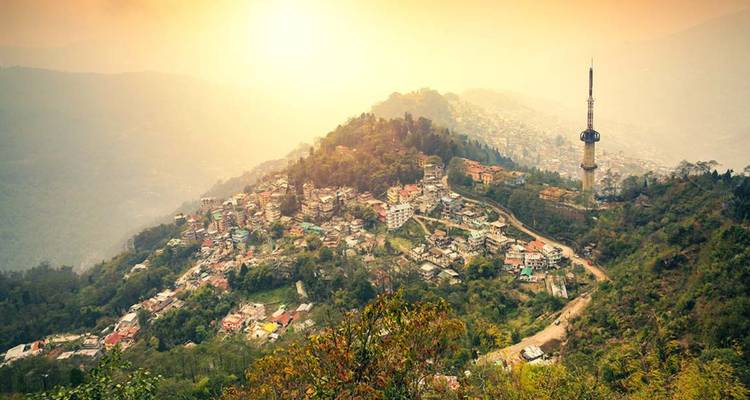 Zonsondergangsgloed over een uitgestrekte bergstad met wazige heuvels en gouden hemel.