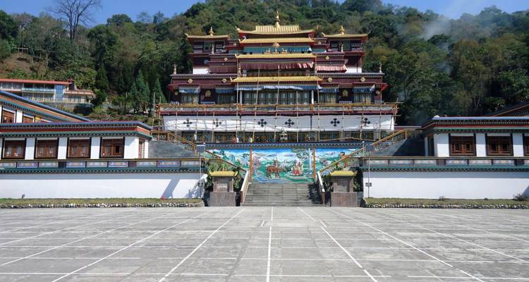 Brede binnenplaats die leidt naar een meerlaags klooster geschilderd in rood en goud met beboste heuvels erachter.