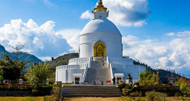 Witte Vrede Pagoda stupa tegen blauwe luchten en berglandschap met een trap die leidt naar de gouden Boeddhanis.
