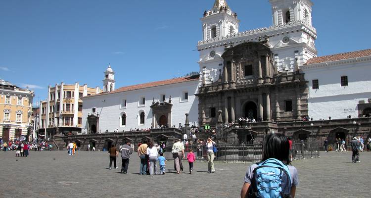 Tourists watching San Francisco Plaza in Quito with colonial church facade.