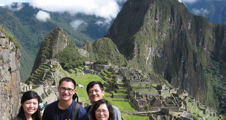 Smiling family posing with Machu Picchu ruins and Huayna Picchu peak behind.